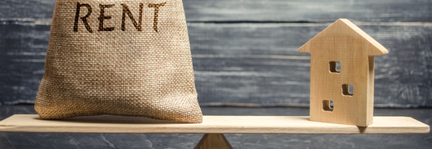 A wooden plank balancing equally with one side having a sack on with the word rent and the other side a wooden block house