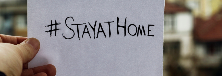 A man's hand holding a piece of paper with "stayathome" handwritten on it