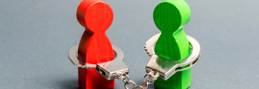 Two wooden playing piece people are handcuffed to each other