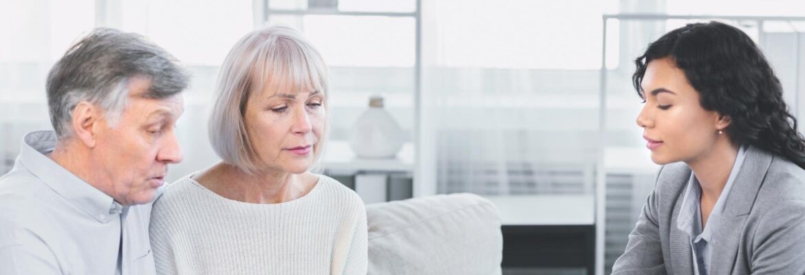 Mature couple sitting on couch, asking about document, signing papers with lawyer