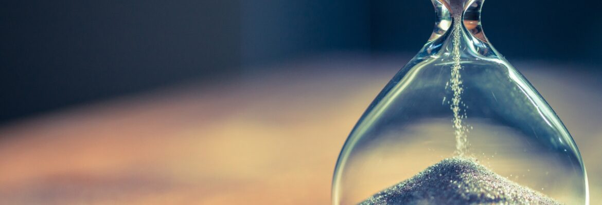 Sand running through the bulbs of an hourglass measuring the passing time in a countdown to a deadline, on a dark background with copy space.
