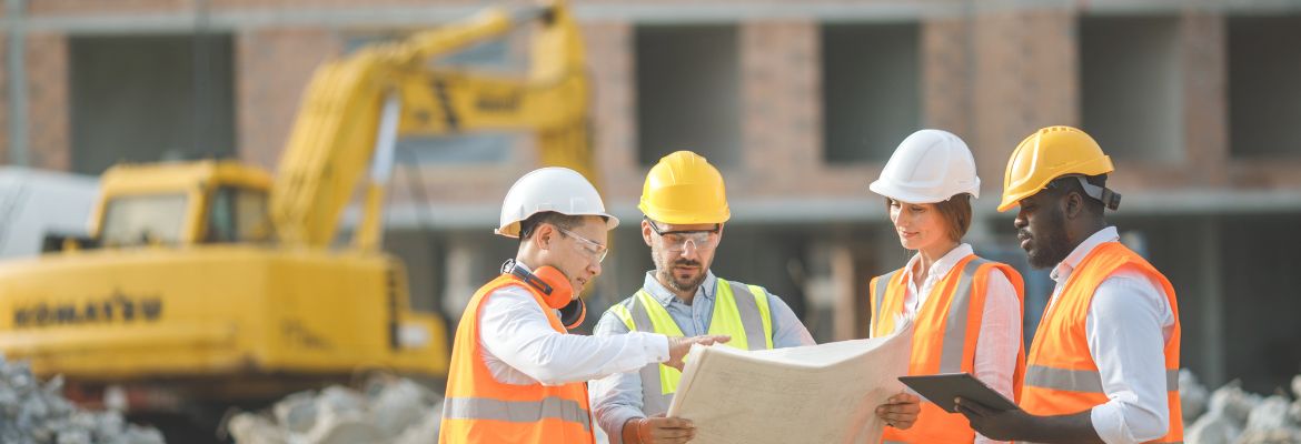 Male and female builders, architect and engineers with draft plan of building and laptop computer talking on constructing site