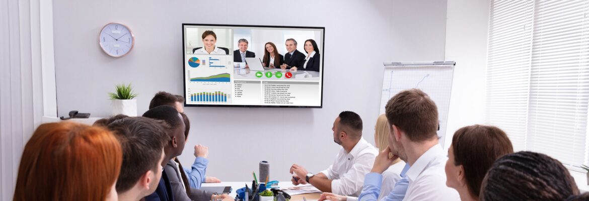 Hybrid meeting - people sitting around a table watching their colleagues join in on a screen