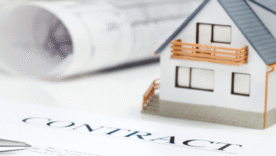 A contract and pen placed beside architect drawings and a house model