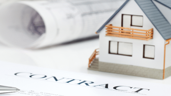 A contract and pen placed beside architect drawings and a house model
